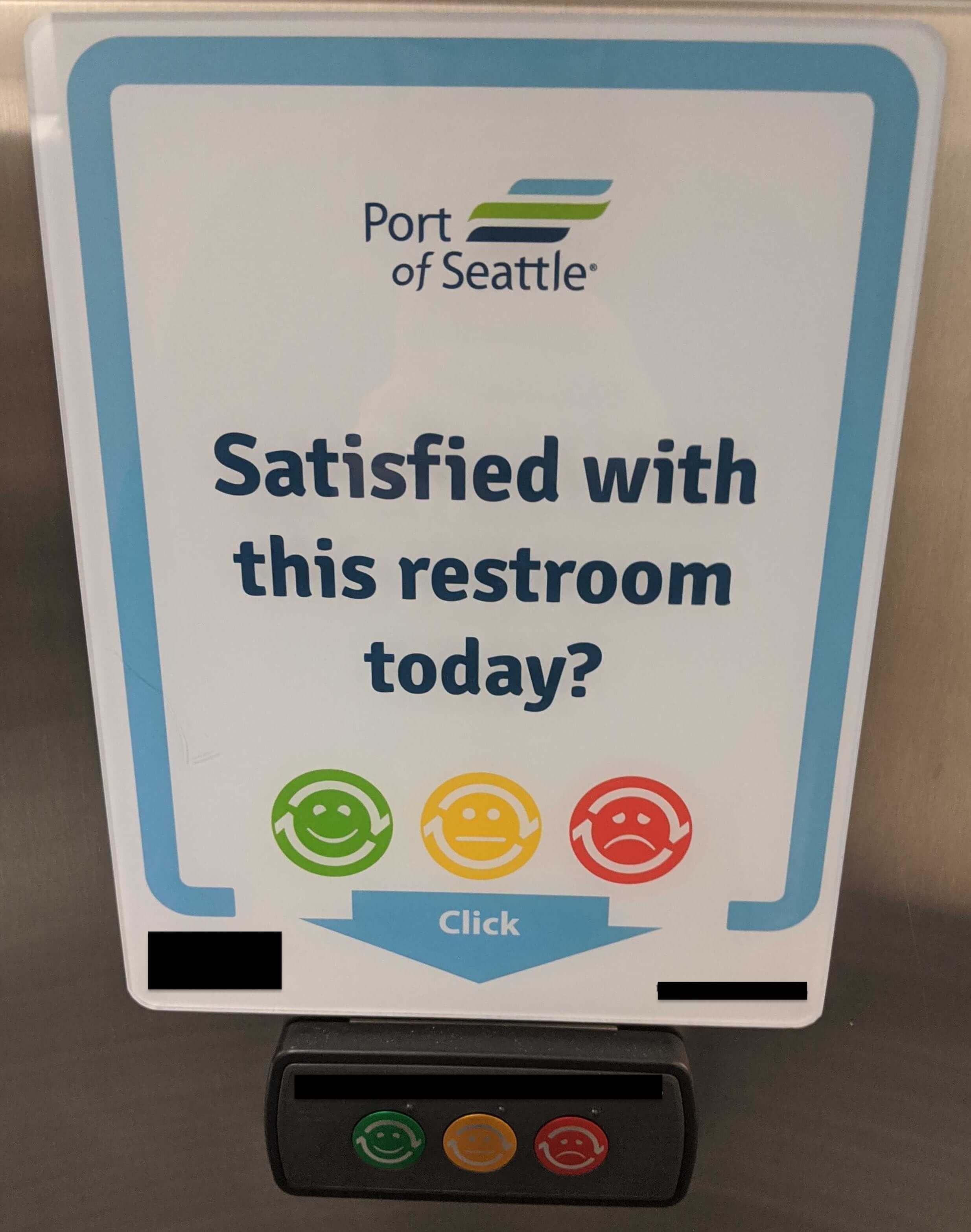 A sign with buttons on a airport bathroom wall asking about the experience